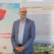 Dr. Sebastian Schiel spricht vor dem Publikum, im Hintergrund eine Präsentationsfolie zum Thema Palliative Care.
