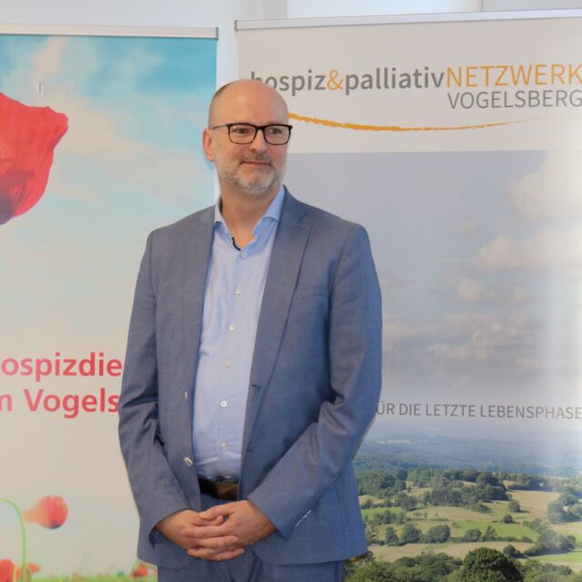 Dr. Sebastian Schiel spricht vor dem Publikum, im Hintergrund eine Präsentationsfolie zum Thema Palliative Care.